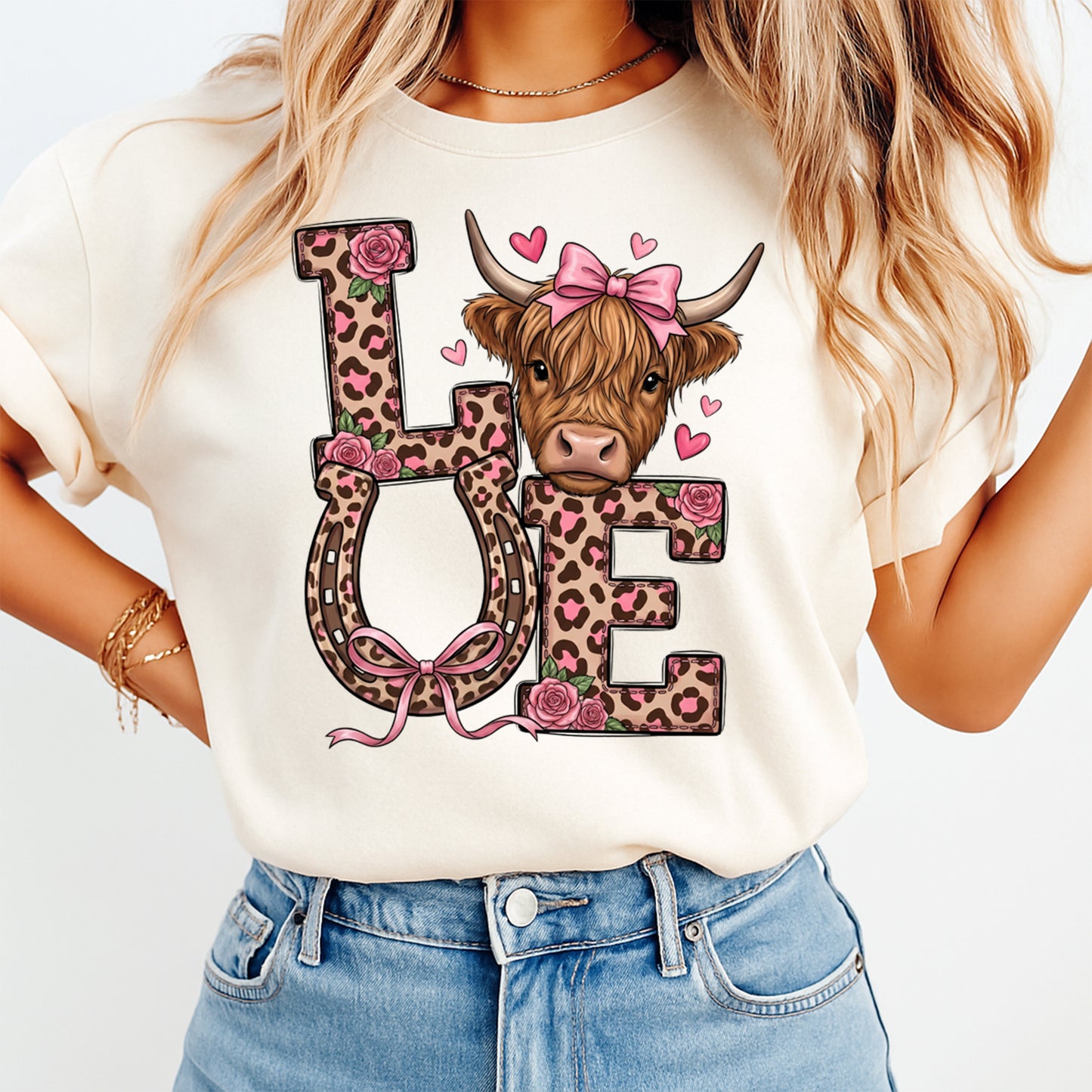Cream t shirt mockup showing Valentine’s Day LOVE leopard letter graphic with highland cow wearing a pink bow, pink hearts, roses, and horseshoe U on the front