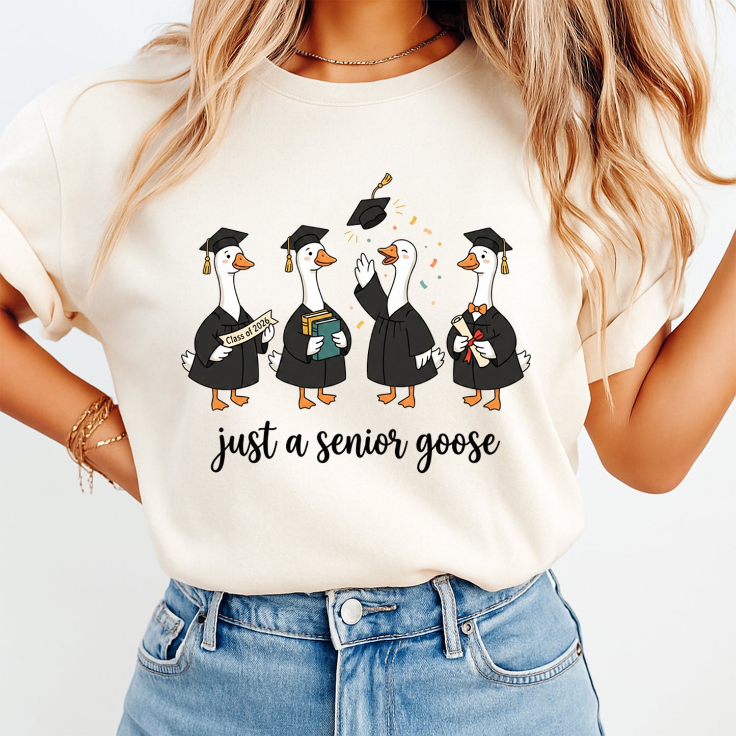 Woman wearing a cream shirt with just a senior goose graduation graphic featuring geese in caps and gowns and class of 2026 details