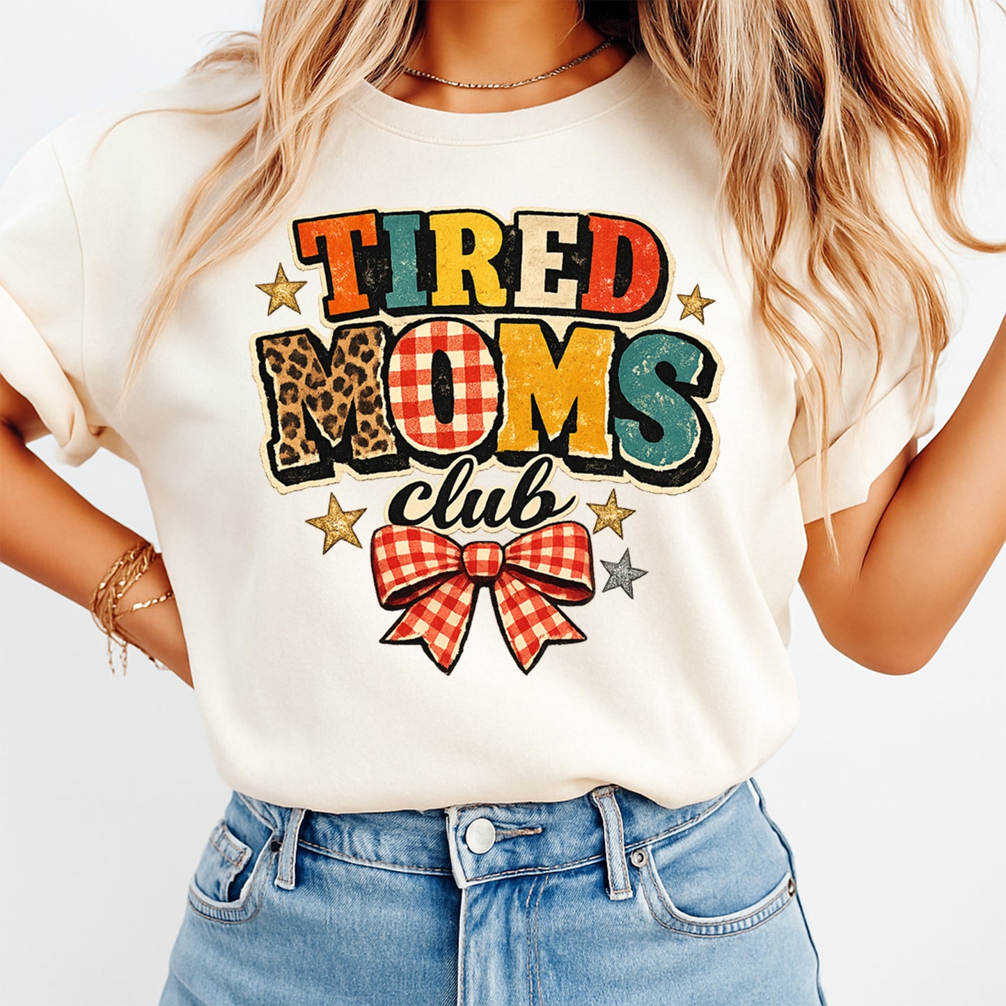 Woman wearing a cream shirt with tired moms club ready to press dtf graphic featuring patchwork lettering gingham bow and star accents