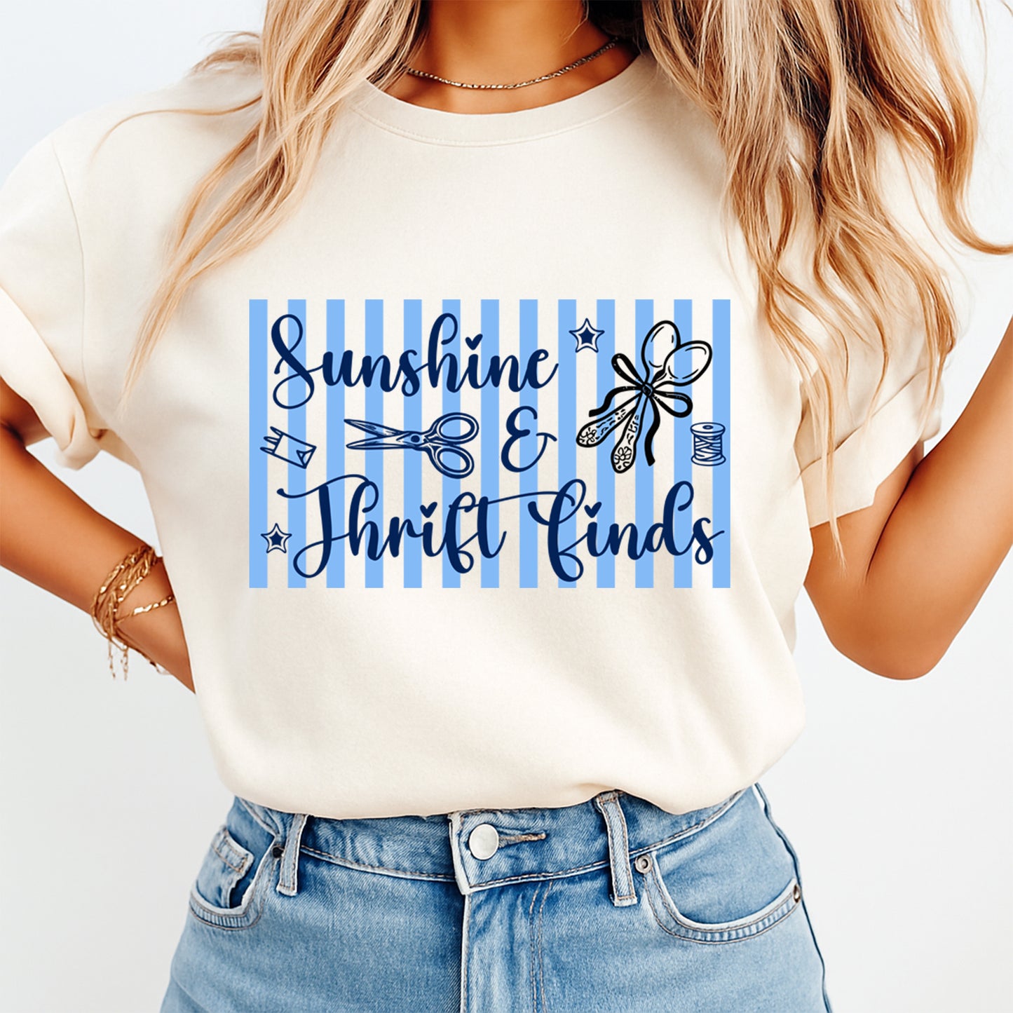 Person wearing a white t-shirt with 'Sunshine & Thrift Finds' text and blue stripes.