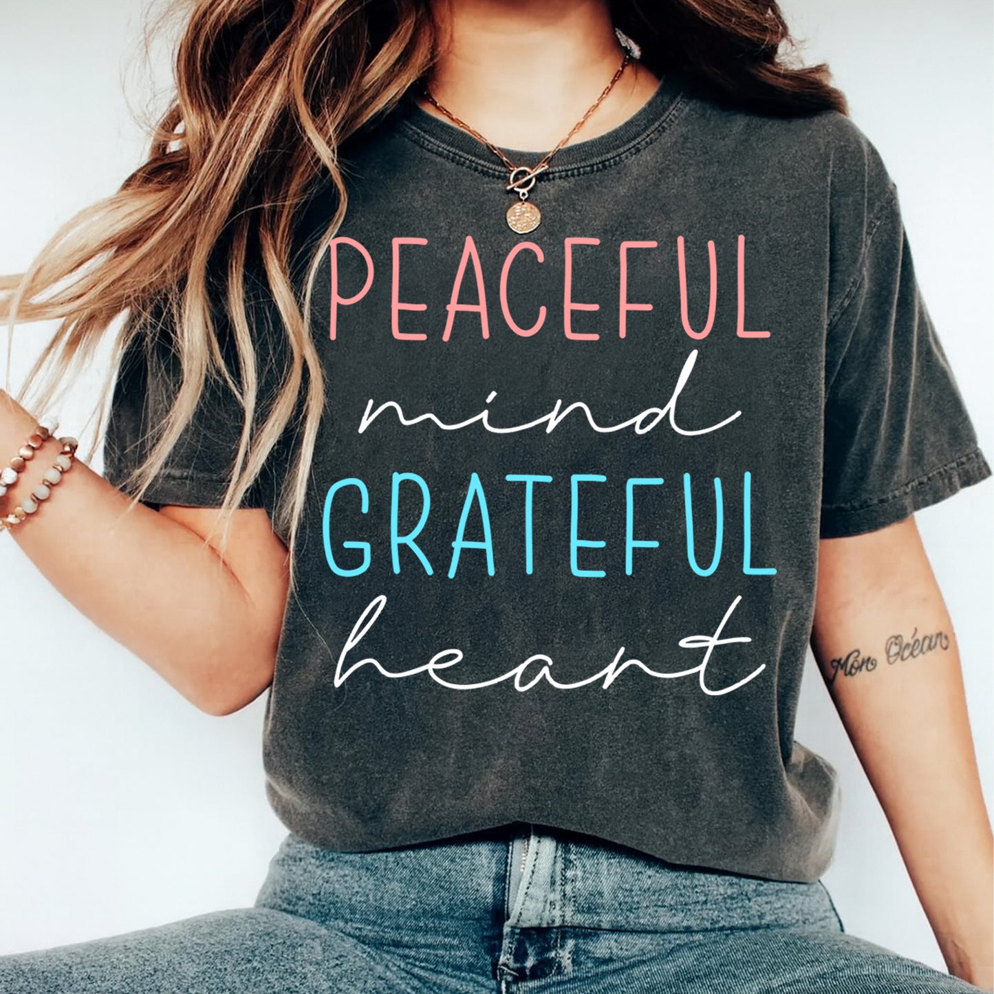 Black shirt mockup featuring an inspirational ready to press dtf transfer with the phrase Peaceful mind Grateful heart in soft pink, teal, and white lettering.