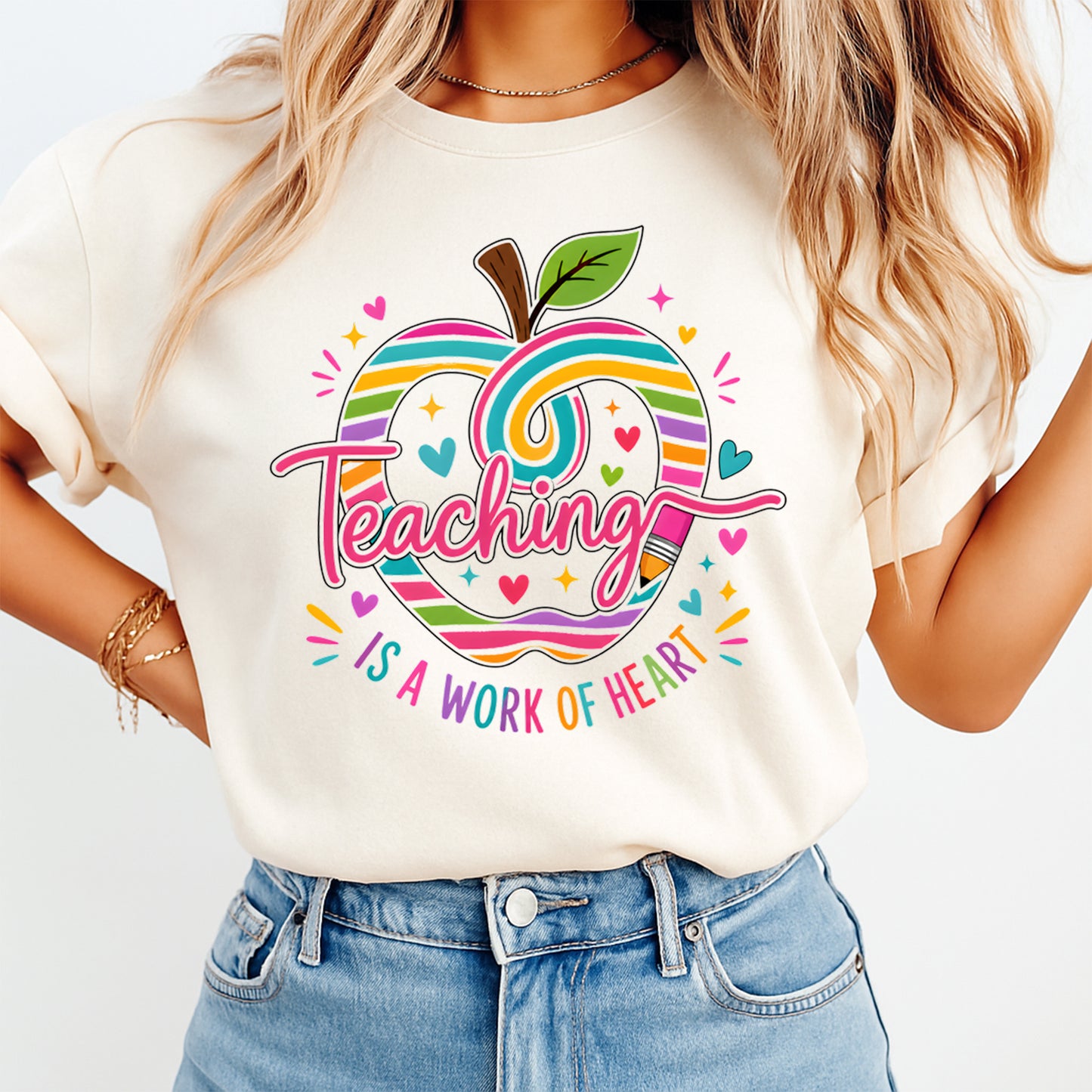 Person wearing a white t-shirt with a colorful apple design and text 'Teaching is a work of heart' on a plain background.