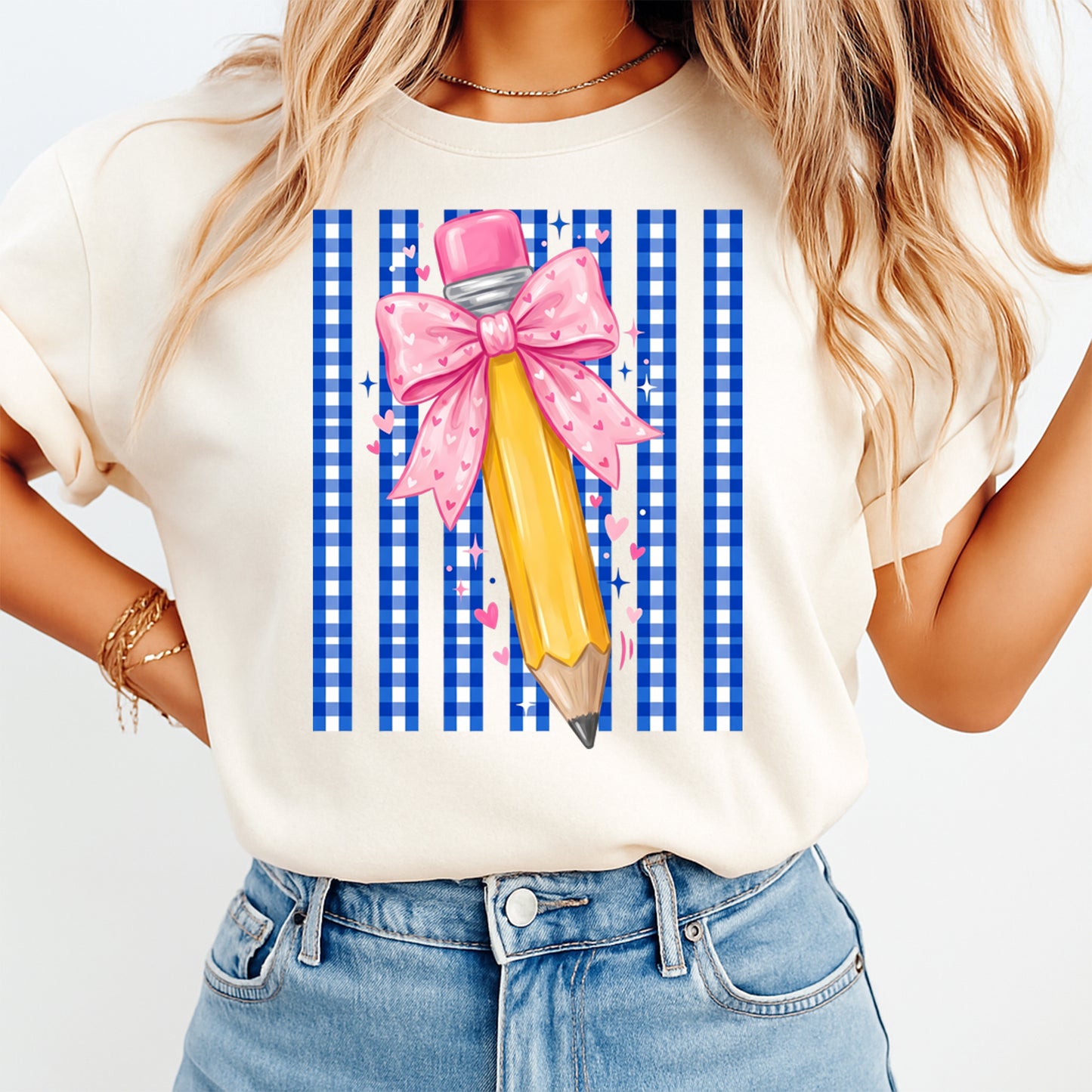 Person wearing a t-shirt with a graphic of a pencil with a pink bow on a blue and white checkered background.