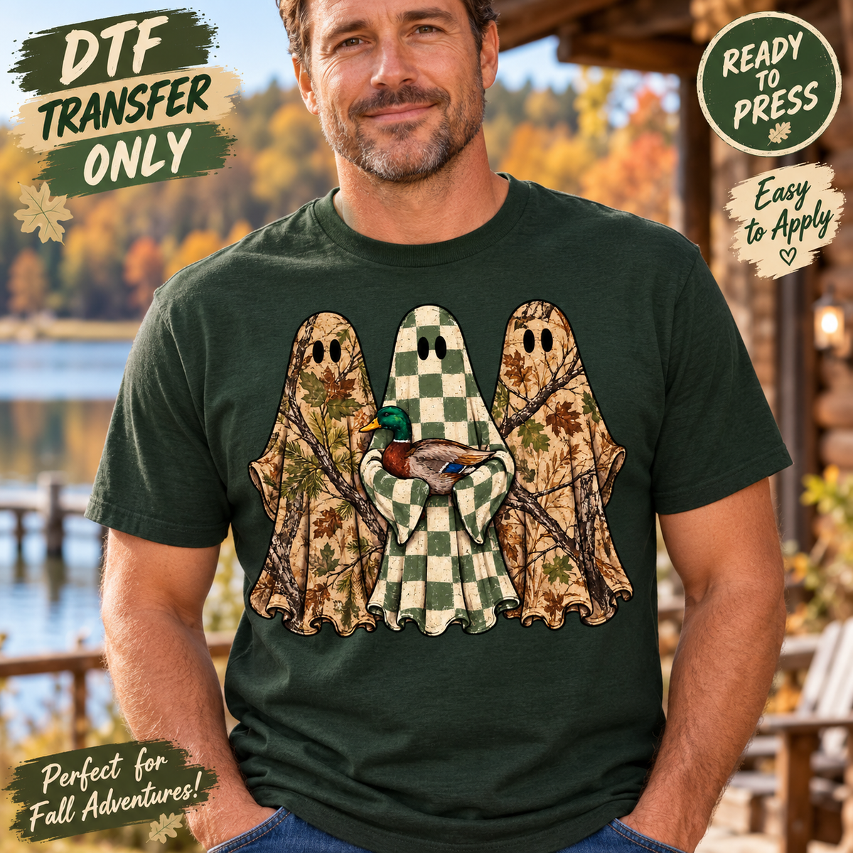 A man wearing a dark forest green t-shirt with a graphic of three ghosts in camouflage and checkered patterns holding a mallard duck. The background is a blurred outdoor lakeside setting.