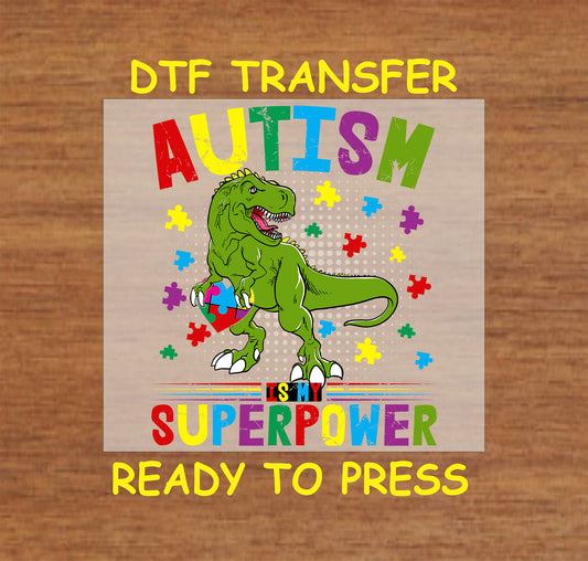 Green dinosaur holding a puzzle piece with "Autism Is My Superpower" text and colorful puzzle pieces, ready-to-press DTF transfer.