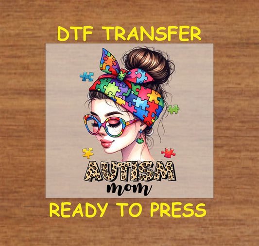 "DTF transfer featuring a colorful puzzle piece bow and glasses with the phrase 'AUTISM Mom' in a bold leopard print font."