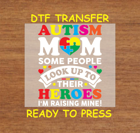 "DTF transfer featuring 'AUTISM MOM' in rainbow colors, a colorful puzzle heart, and the phrase 'Some people look up to their heroes, I'm raising mine!'"