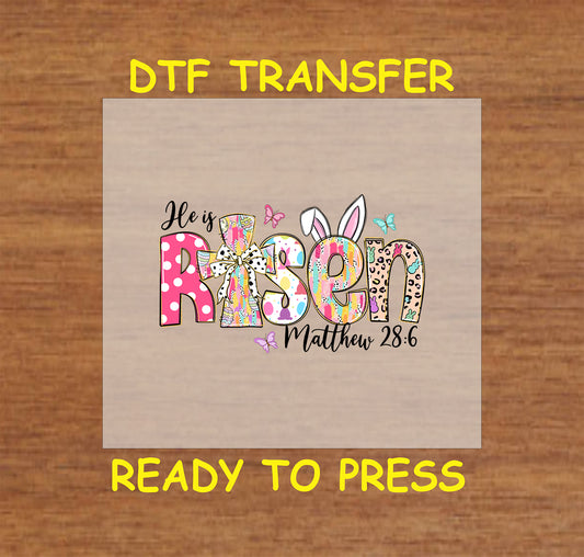 Colorful "He Is Risen" text with bunny ears, a cross bow, and butterflies, featuring Matthew 28:6.