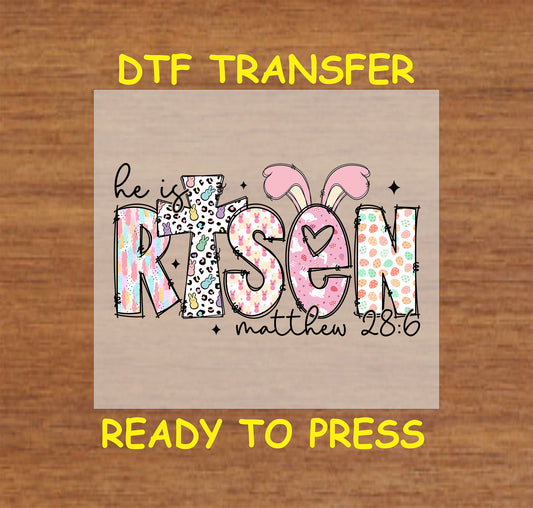 Easter DTF transfer with "He Is Risen" in patterned text, bunny ears, and Matthew 28:6 verse.