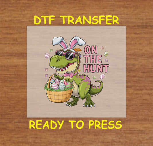 Easter DTF transfer with a T-Rex wearing bunny ears and sunglasses, carrying a basket of eggs with "On The Hunt" text.