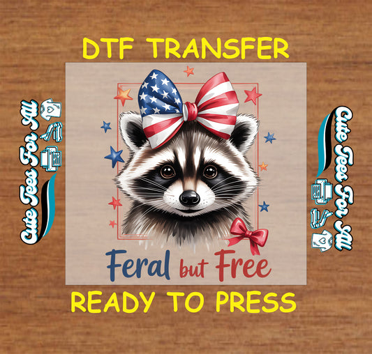DTF transfer of raccoon with patriotic bow and text “Feral but Free” surrounded by red, white, and blue stars.