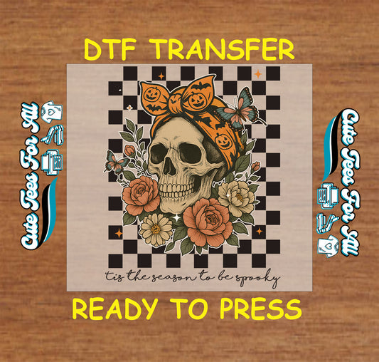 Skull with pumpkin headwrap surrounded by flowers and butterflies on checkerboard background

