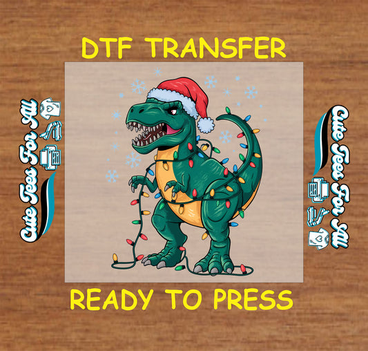 Christmas DTF transfer with green T-Rex dinosaur in Santa hat wrapped in holiday lights and snowflakes, ready to press dtf heat transfer for diy shirts