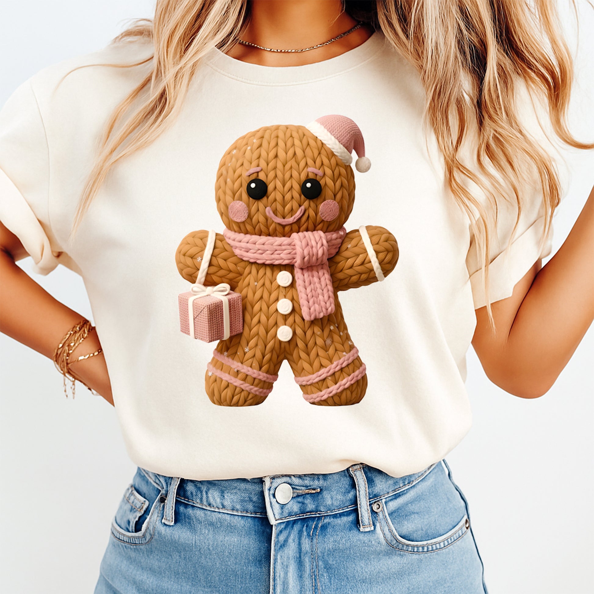 Person wearing a white t-shirt with a gingerbread man design, holding a small gift box.