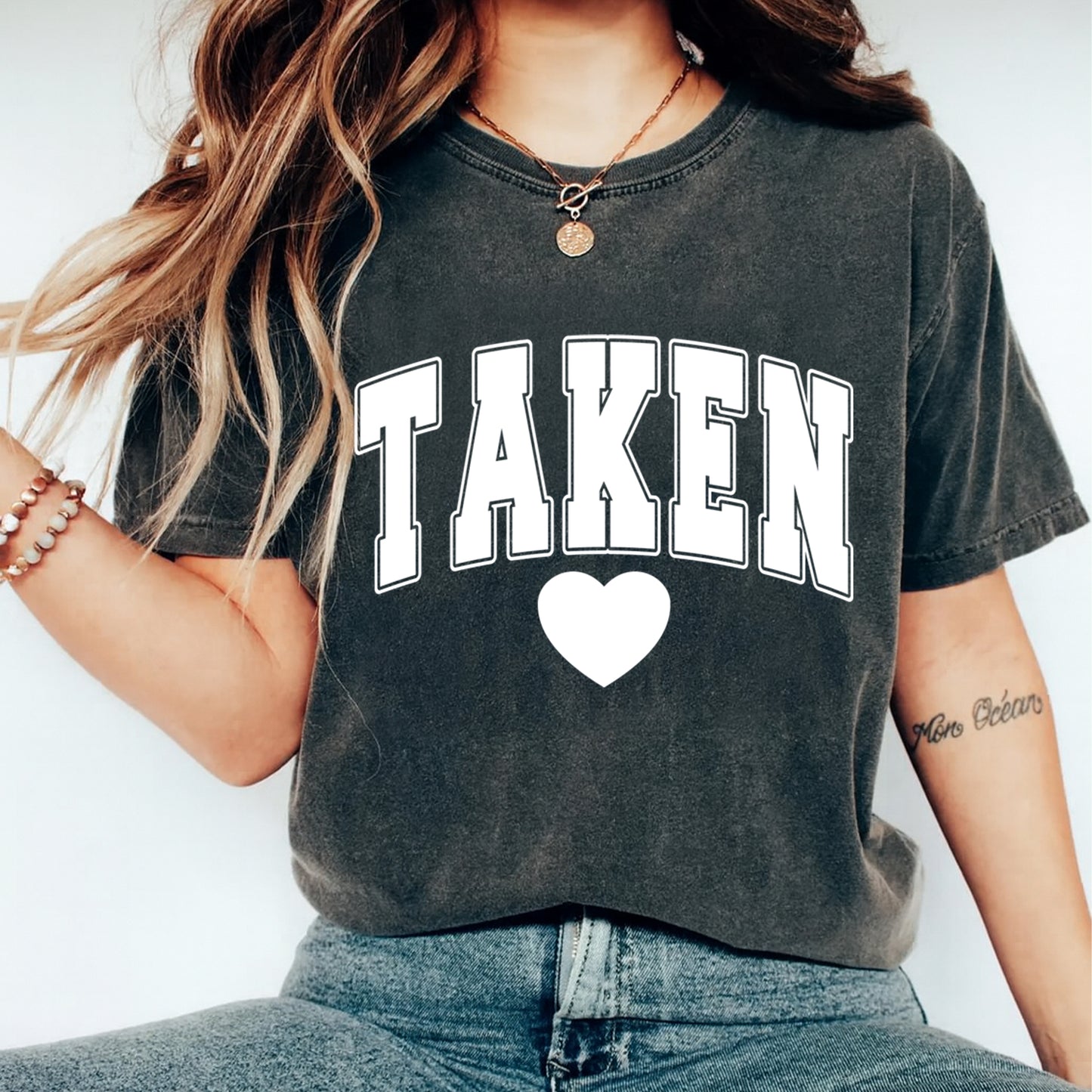 Person wearing a black t-shirt with 'TAKEN' and a heart on a white background