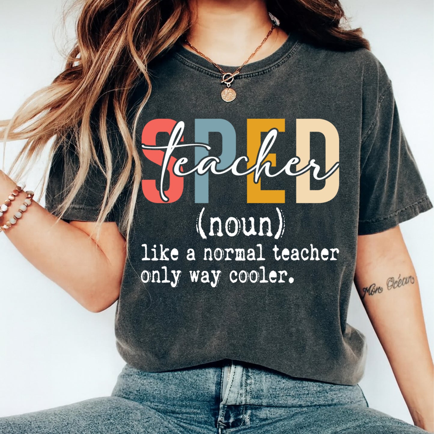 Dark gray t shirt mockup showing the text SPED teacher like a normal teacher only way cooler in multicolor lettering, teacher graphic tee