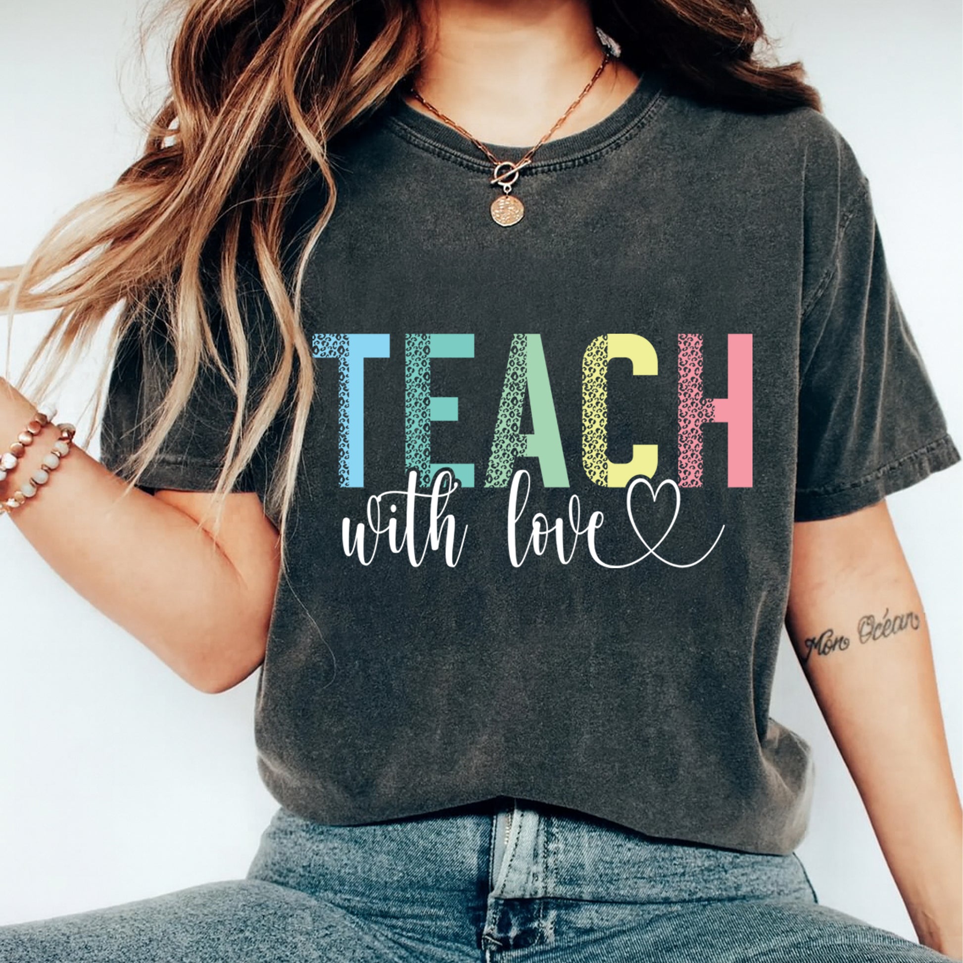 Dark gray t shirt mockup showing the text Teach with love in multicolor lettering with script detail, teacher graphic tee