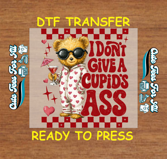 Ready to press dtf Valentine transfer with I Don’t Give a Cupid’s Ass text, sarcastic bear illustration, heart pajamas, cocktail glass, and red Valentine accents