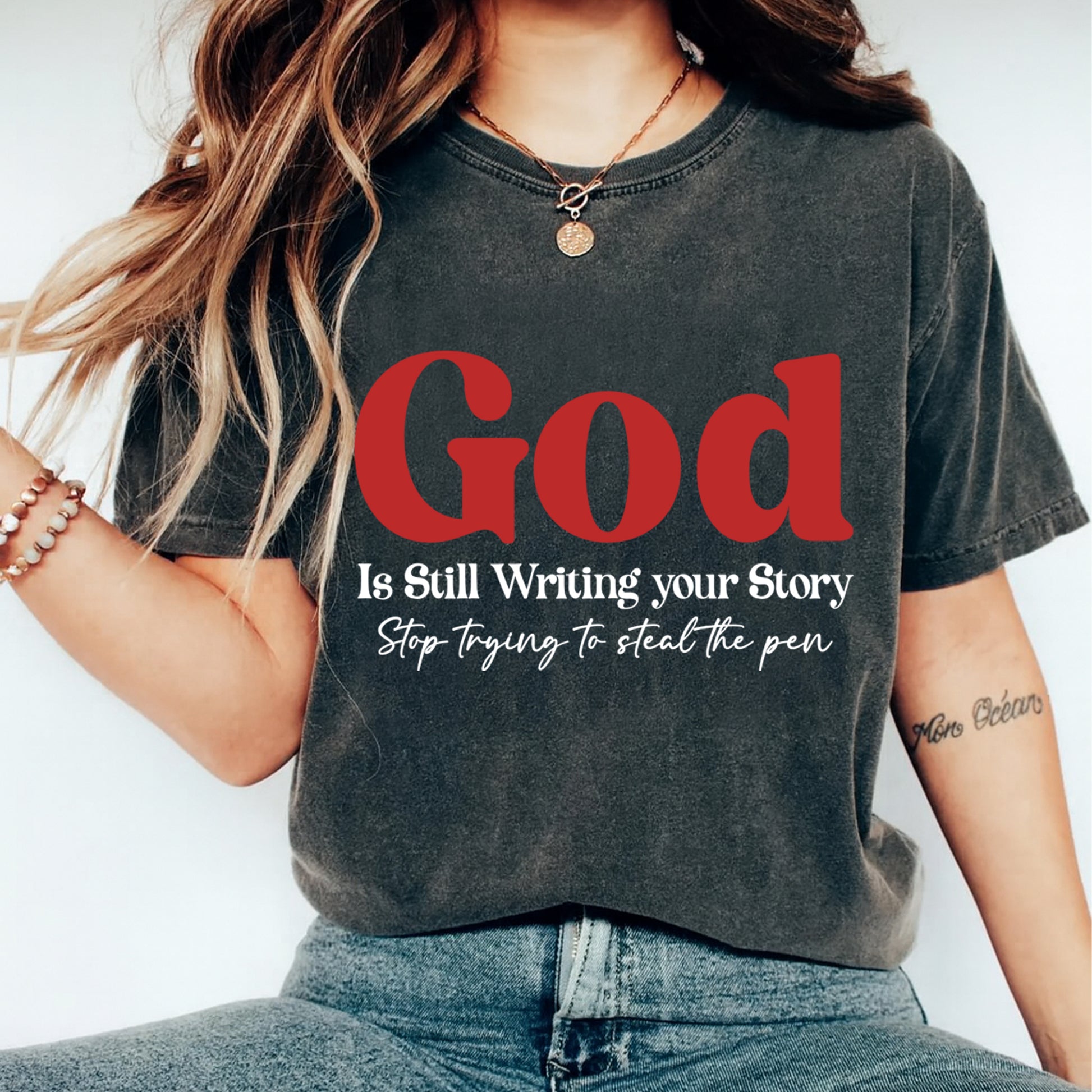 God is still writing your story inspirational quote graphic pressed on a dark t shirt showing bold faith typography