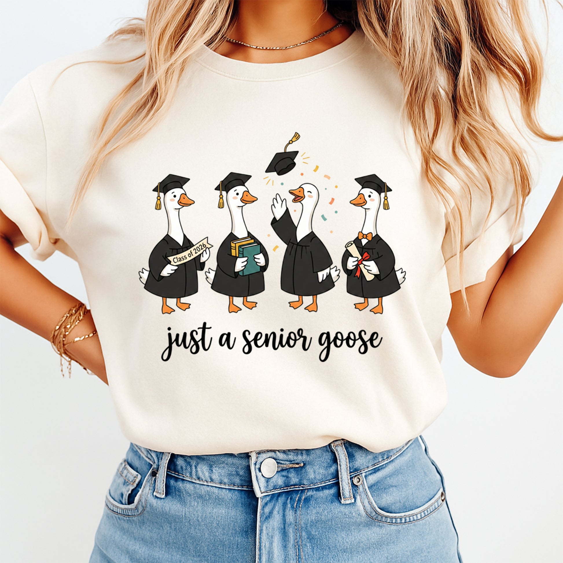 Woman wearing a cream shirt with just a senior goose graduation graphic featuring geese in caps and gowns and class of 2026 details