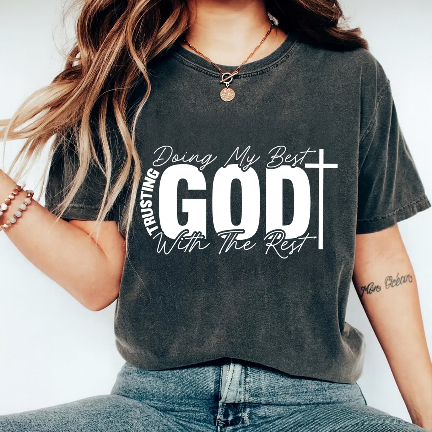 Woman wearing a dark shirt with doing my best trusting God with the rest ready to press dtf graphic in white faith lettering with a cross
