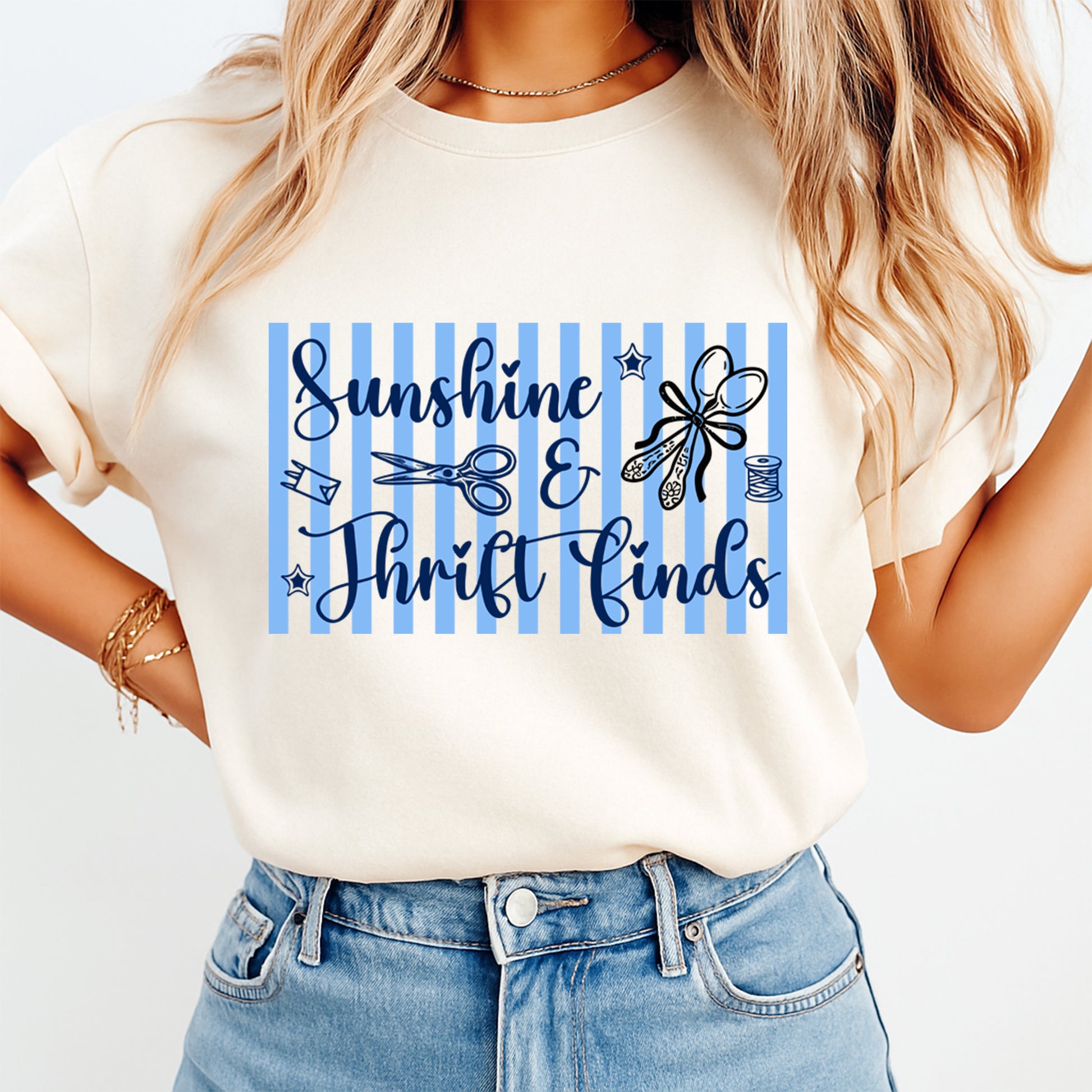 Person wearing a white t-shirt with 'Sunshine & Thrift Finds' text and blue stripes.