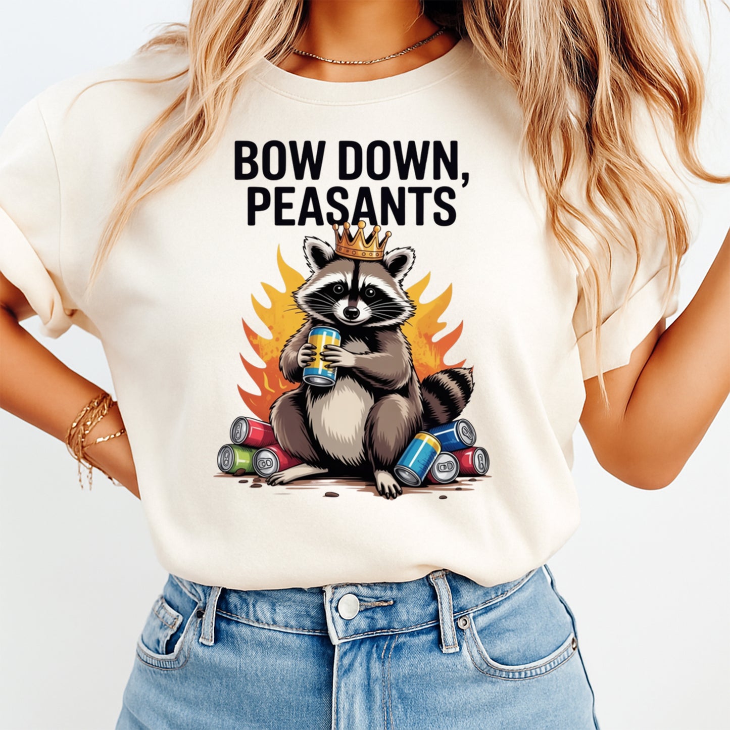 Woman wearing a cream shirt with a funny crowned raccoon ready to press dtf graphic with flames and Bow Down Peasants text