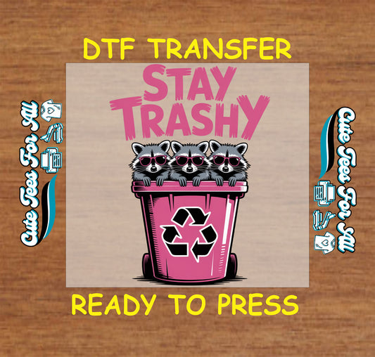 Funny raccoon ready to press dtf transfer with Stay Trashy text, three raccoons in pink sunglasses, and a pink recycling bin on a wood background