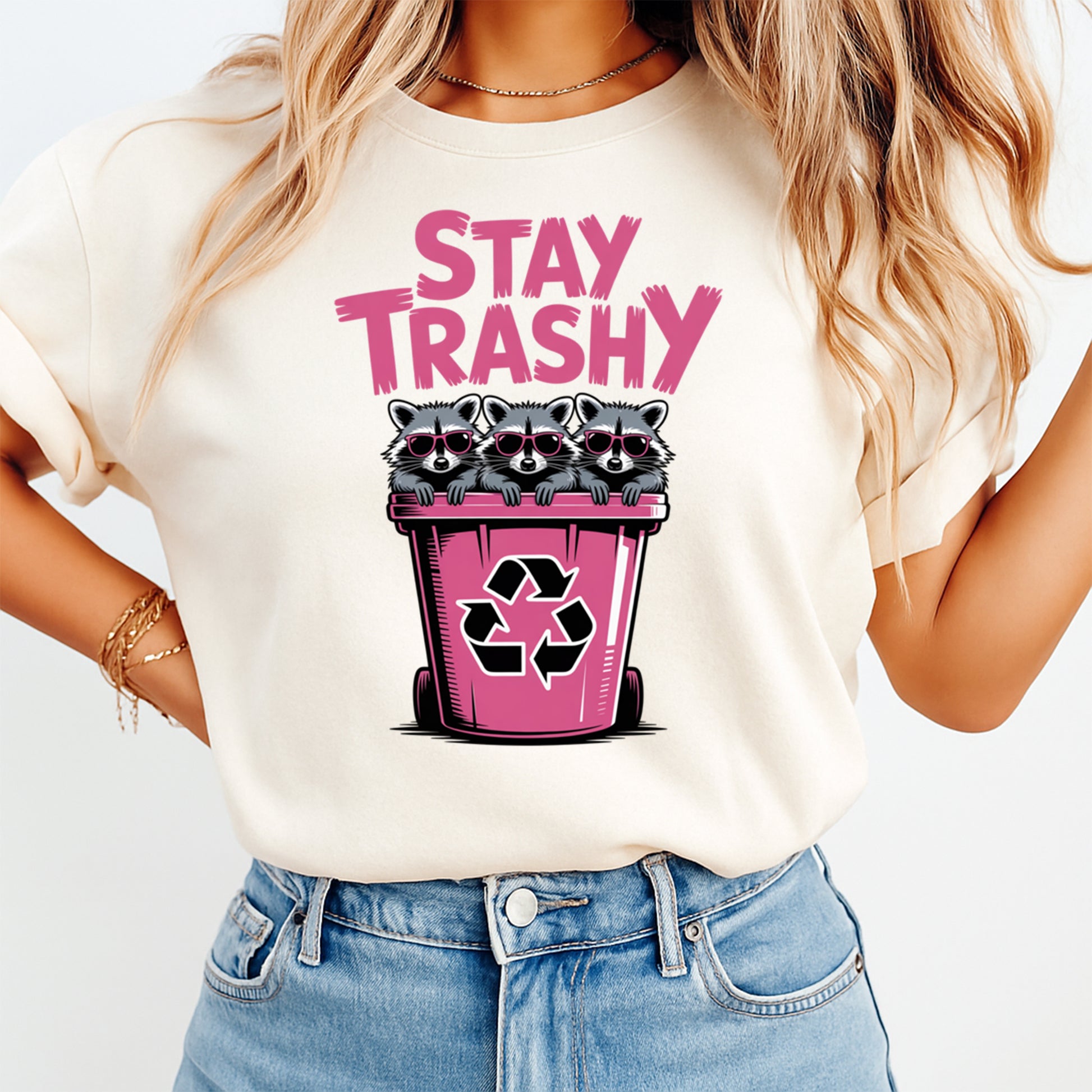 Woman wearing a cream shirt with a funny raccoon ready to press dtf graphic featuring Stay Trashy text and three raccoons in a pink recycling bin