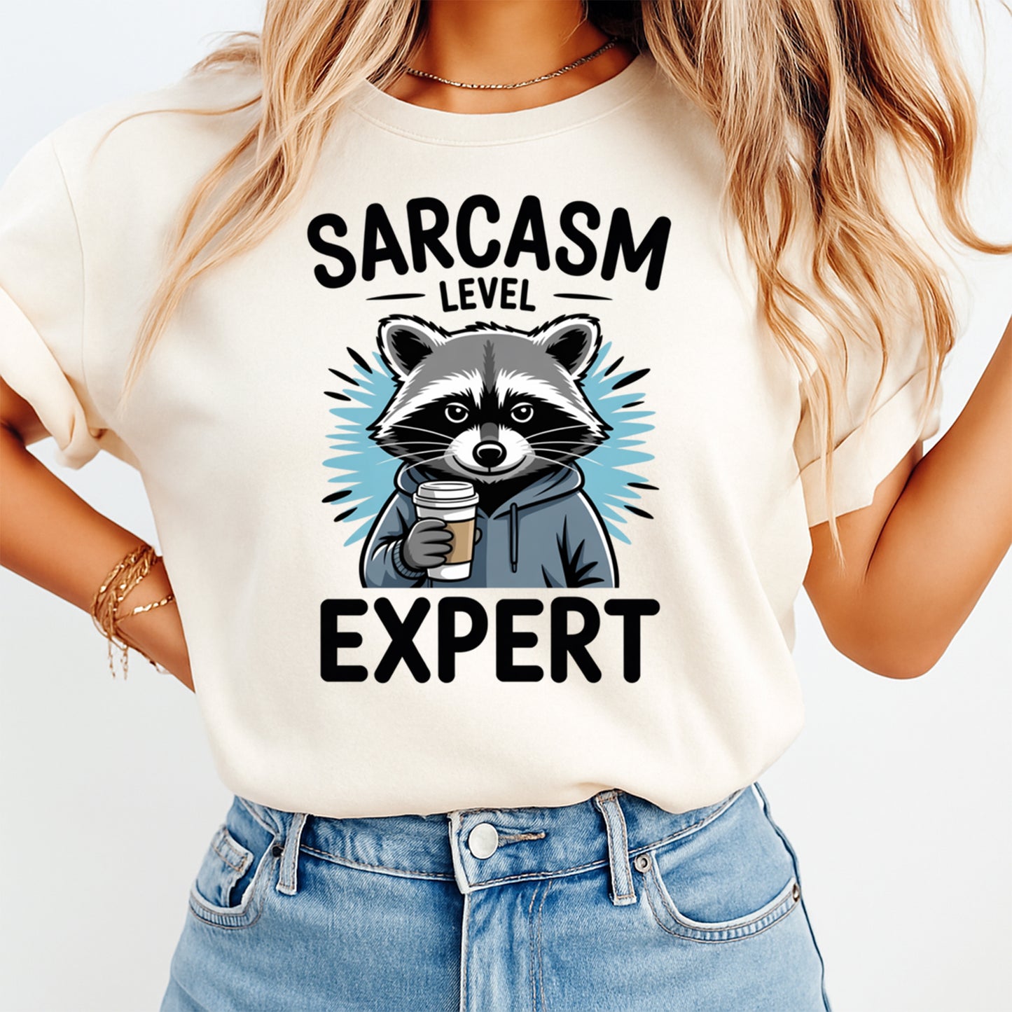 Woman wearing a cream shirt with a funny raccoon ready to press dtf graphic featuring Sarcasm Level Expert text and a coffee cup