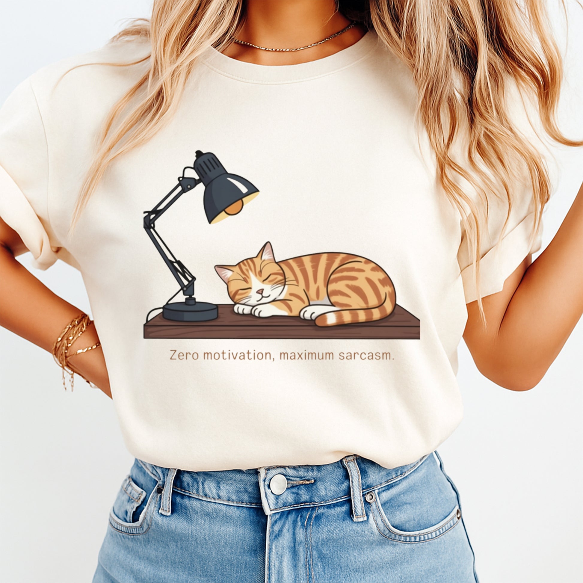 Woman wearing a cream shirt with a sarcastic sleeping orange cat under a desk lamp and the quote zero motivation maximum sarcasm