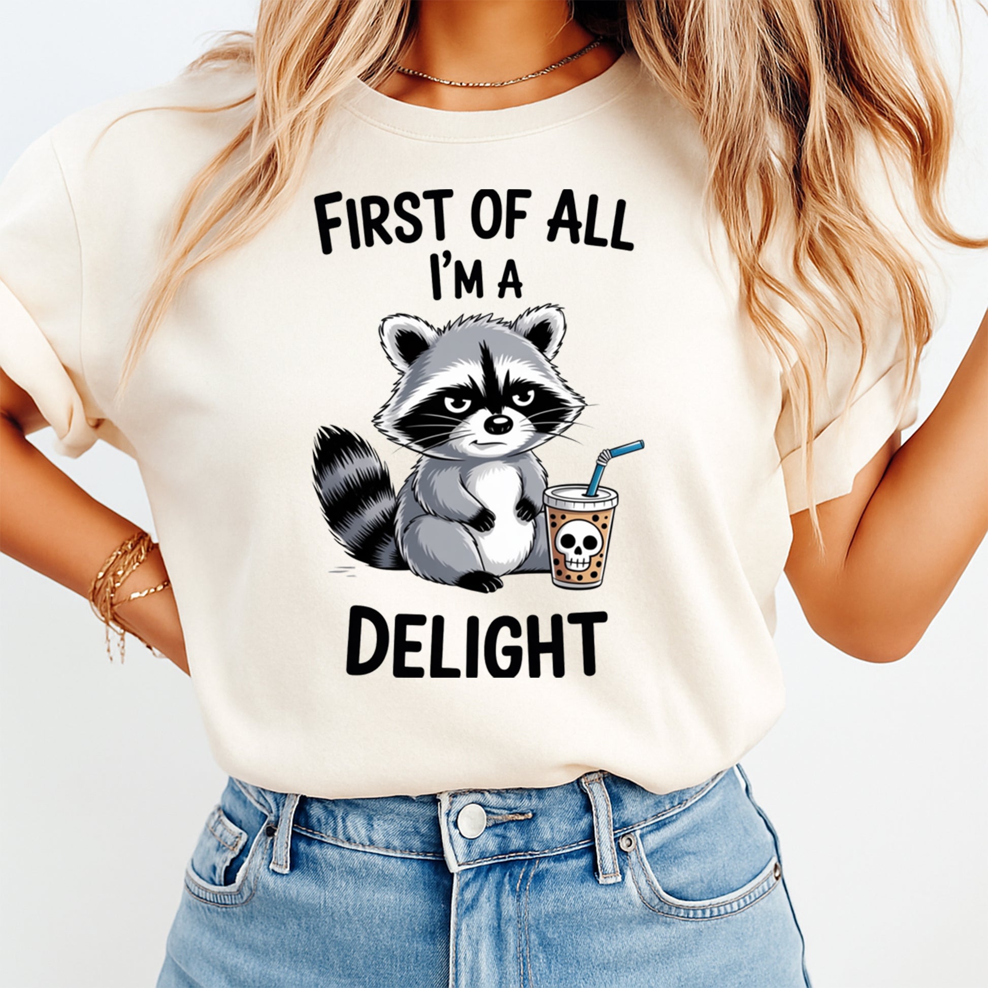 Mockup shirt featuring a grumpy raccoon beside a drink cup with a skull graphic and the phrase First Of All Im a Delight
