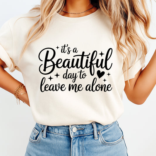 Mockup image of a cream shirt featuring the phrase it’s a Beautiful day to leave me alone in black script with small stars and a heart