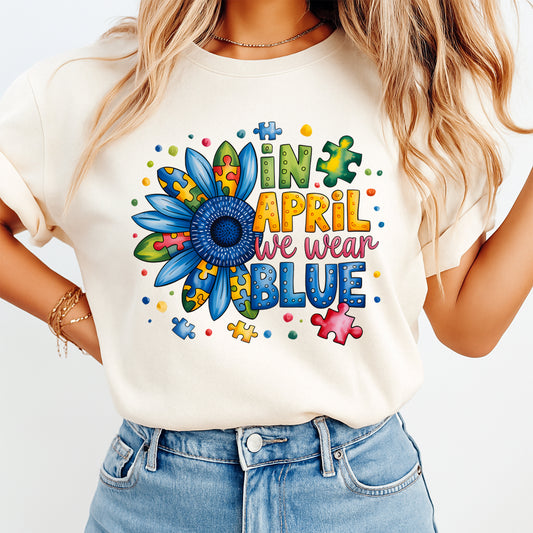 Mockup of a cream shirt featuring an autism awareness ready to press dtf transfer with the phrase In April We Wear Blue, colorful sunflower, and puzzle-piece details.