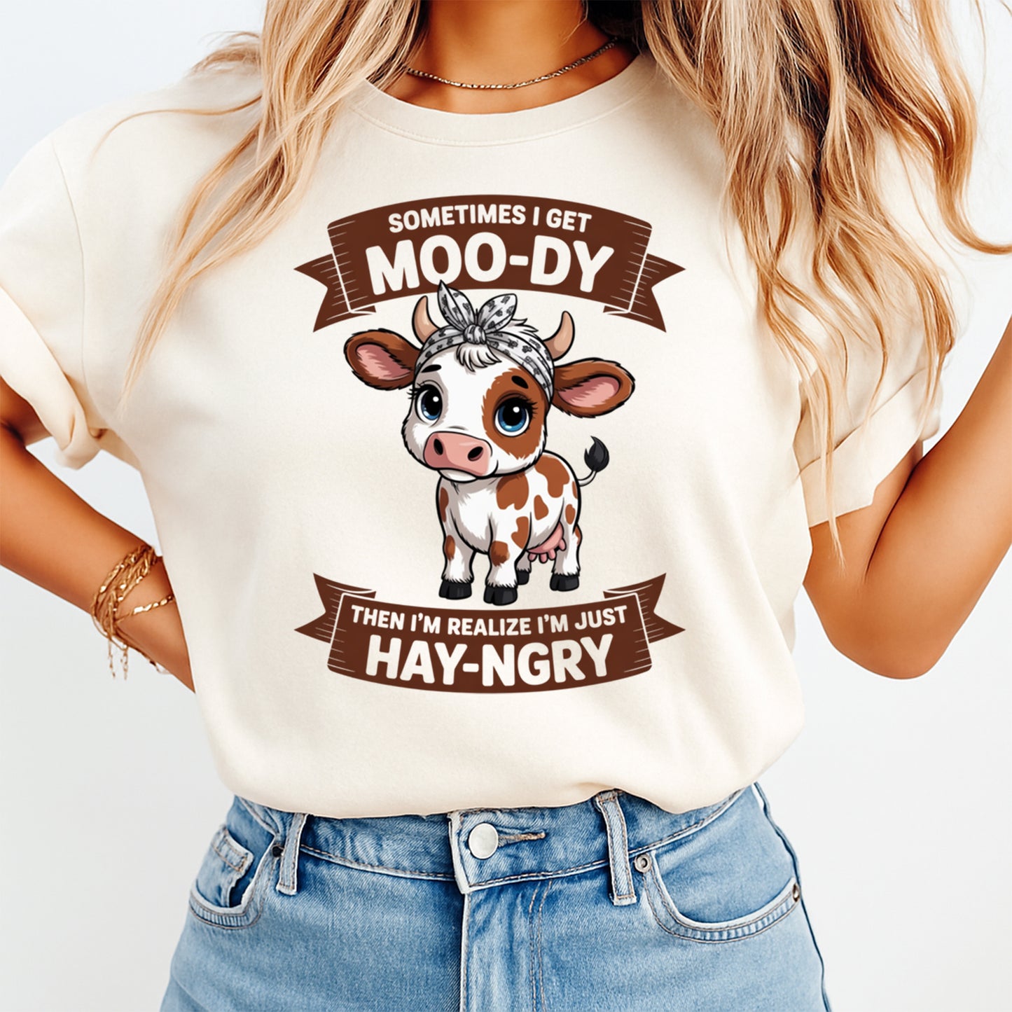 Mockup of a cream shirt featuring a funny cow ready to press dtf transfer with the phrase Sometimes I get Moo-dy then I’m realize I’m just Hay-ngry.