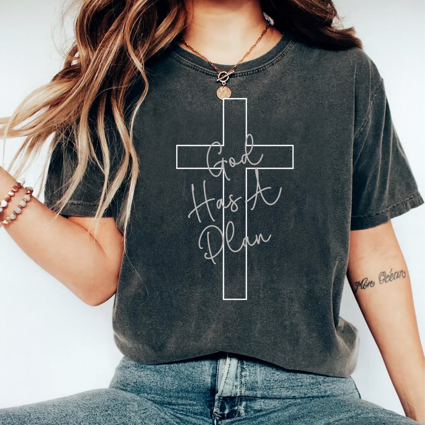 Black shirt mockup featuring a faith ready to press dtf transfer with a white cross outline and the phrase God Has A Plan in soft script lettering.