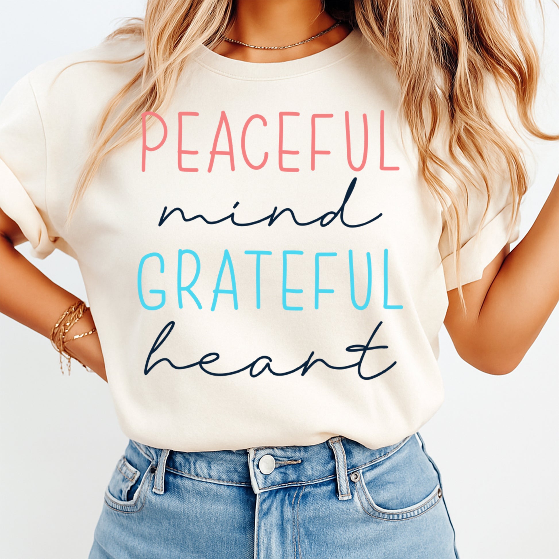 Cream shirt mockup featuring an inspirational ready to press dtf transfer with the phrase Peaceful mind Grateful heart in soft pink, blue, and navy lettering.