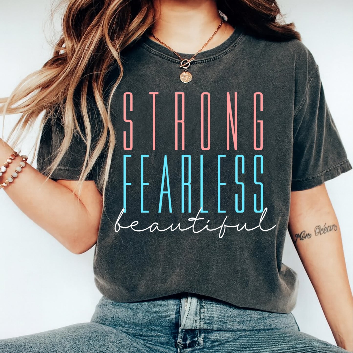 Person wearing a t-shirt with 'STRONG FEARLESS beautiful' text on a plain background