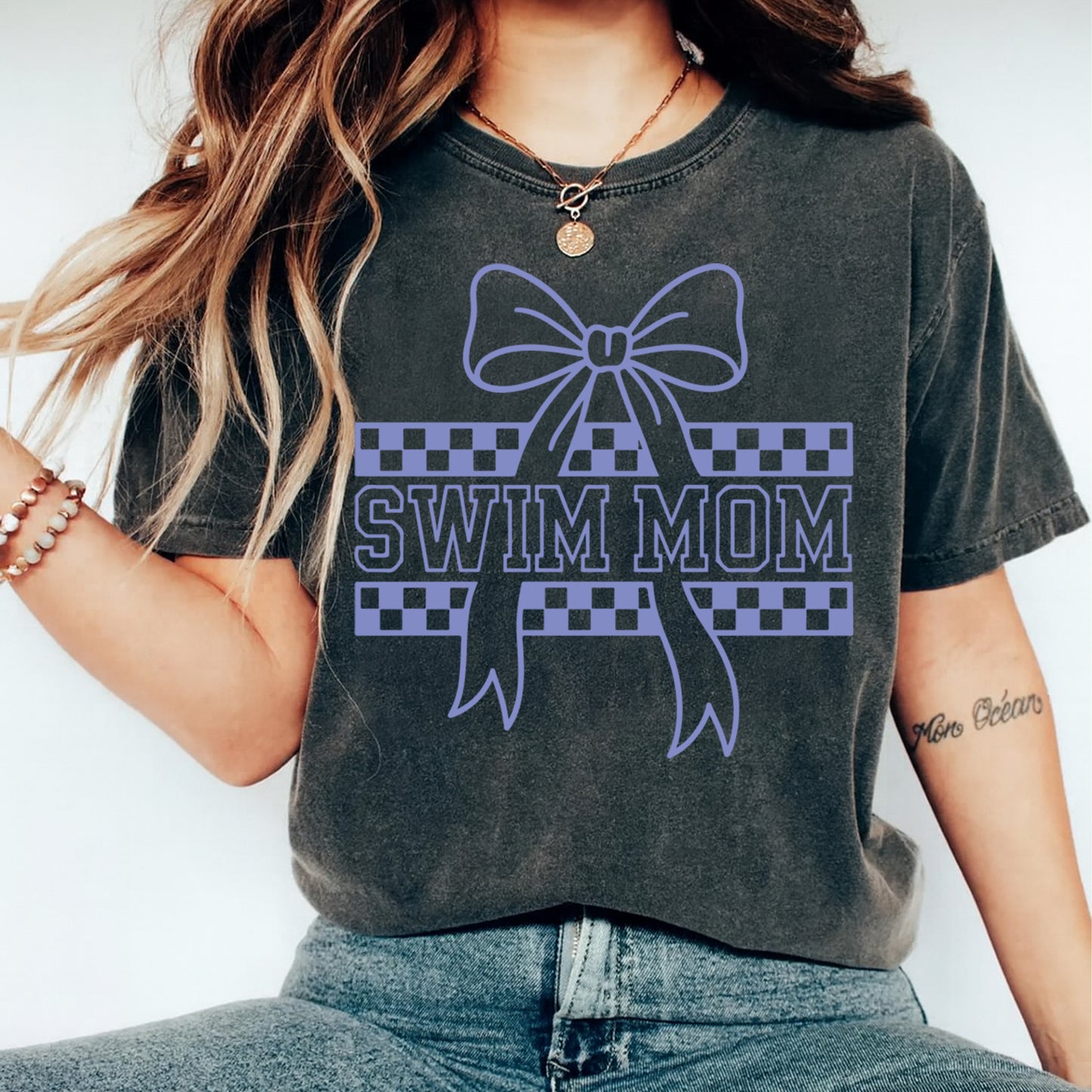 Lifestyle mockup of a black shirt with a swim mom ready to press dtf graphic featuring a bow and checkered ribbon details.