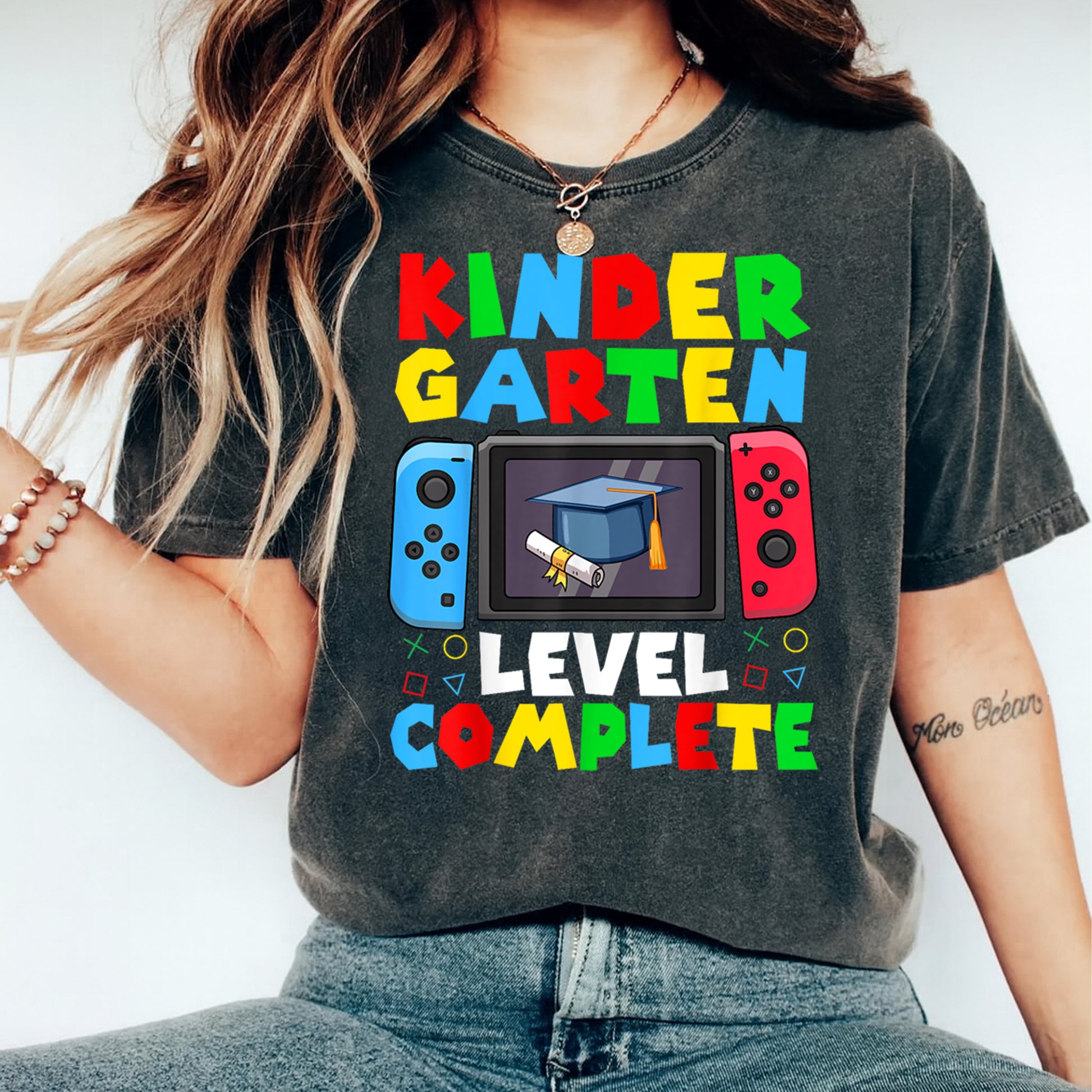 Mockup of black shirt featuring Kindergarten Level Complete ready to press dtf transfer with colorful gamer graduation artwork.