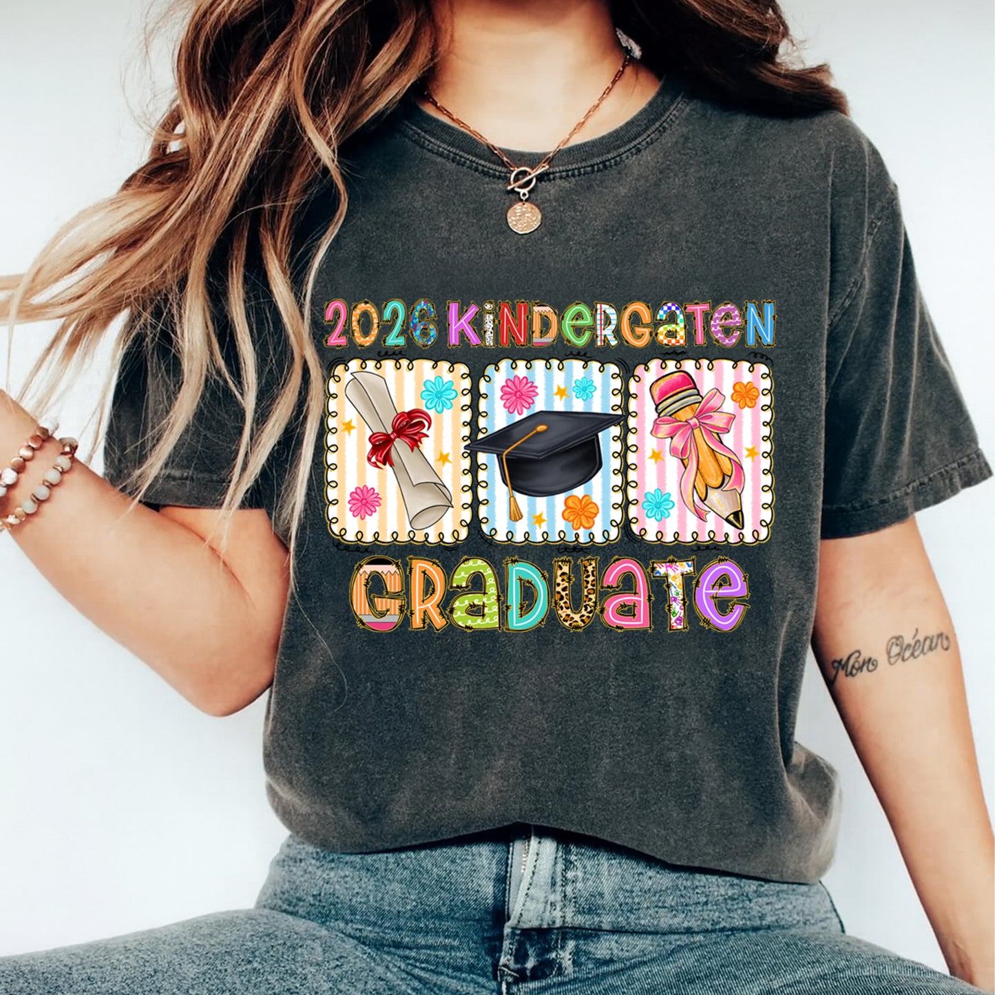 Mockup of black shirt featuring colorful 2026 Kindergarten Graduate ready to press dtf transfer with diploma, graduation cap, and pencil artwork.