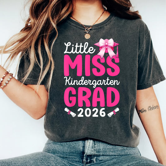 Black shirt mockup featuring a pink kindergarten grad 2026 ready to press dtf transfer with bow, graduation cap, and diploma accents.