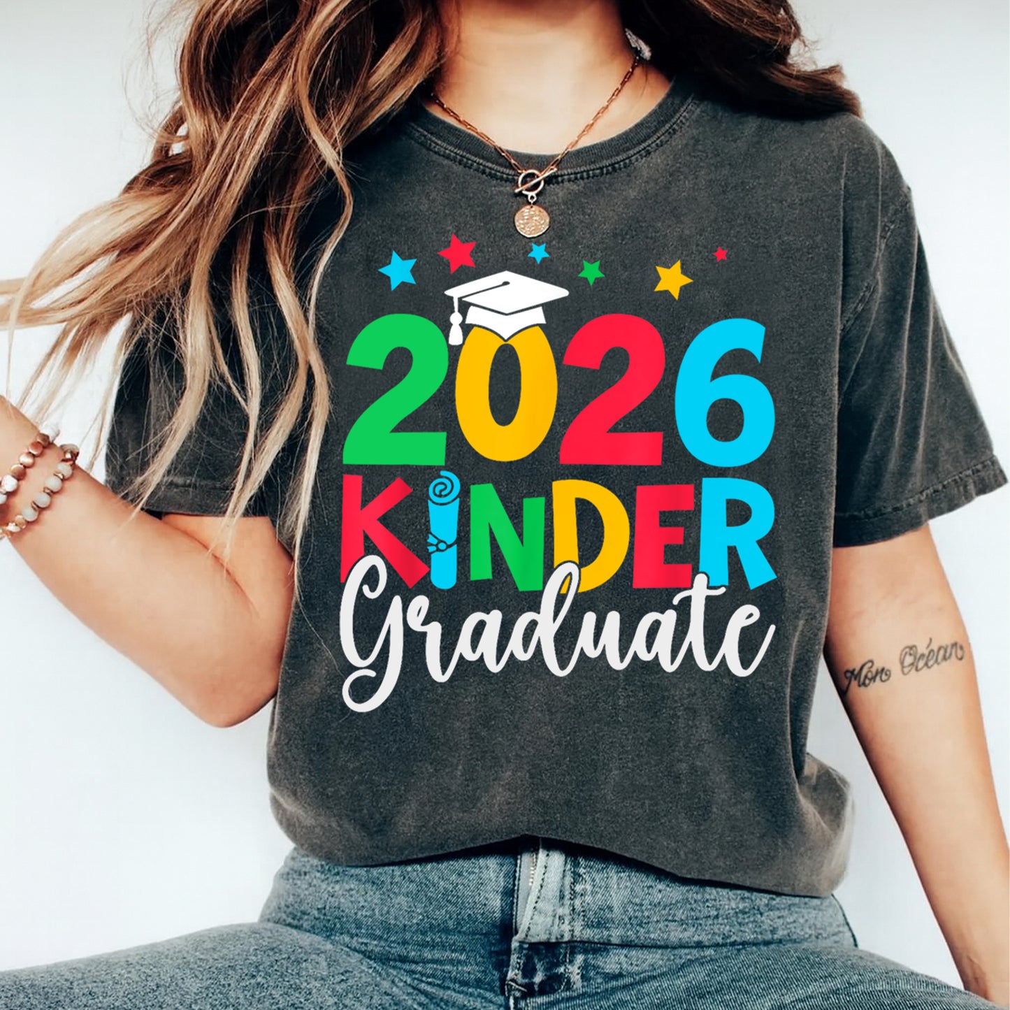 Black shirt mockup featuring a 2026 Kinder Graduate ready to press dtf transfer with colorful lettering, graduation cap, diploma detail, and stars.