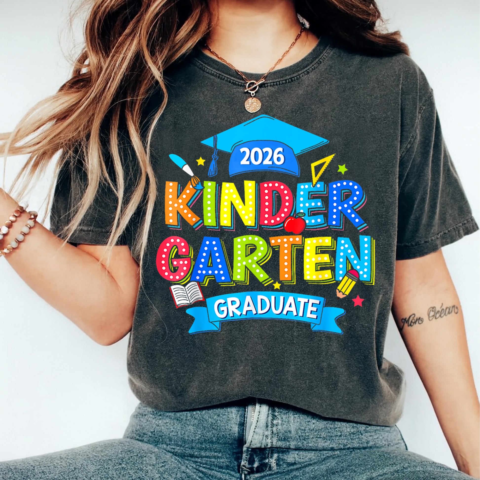 Black shirt mockup featuring a Kinder Garten Graduate 2026 ready to press dtf transfer with colorful letters, graduation cap, school supplies, and blue banner.