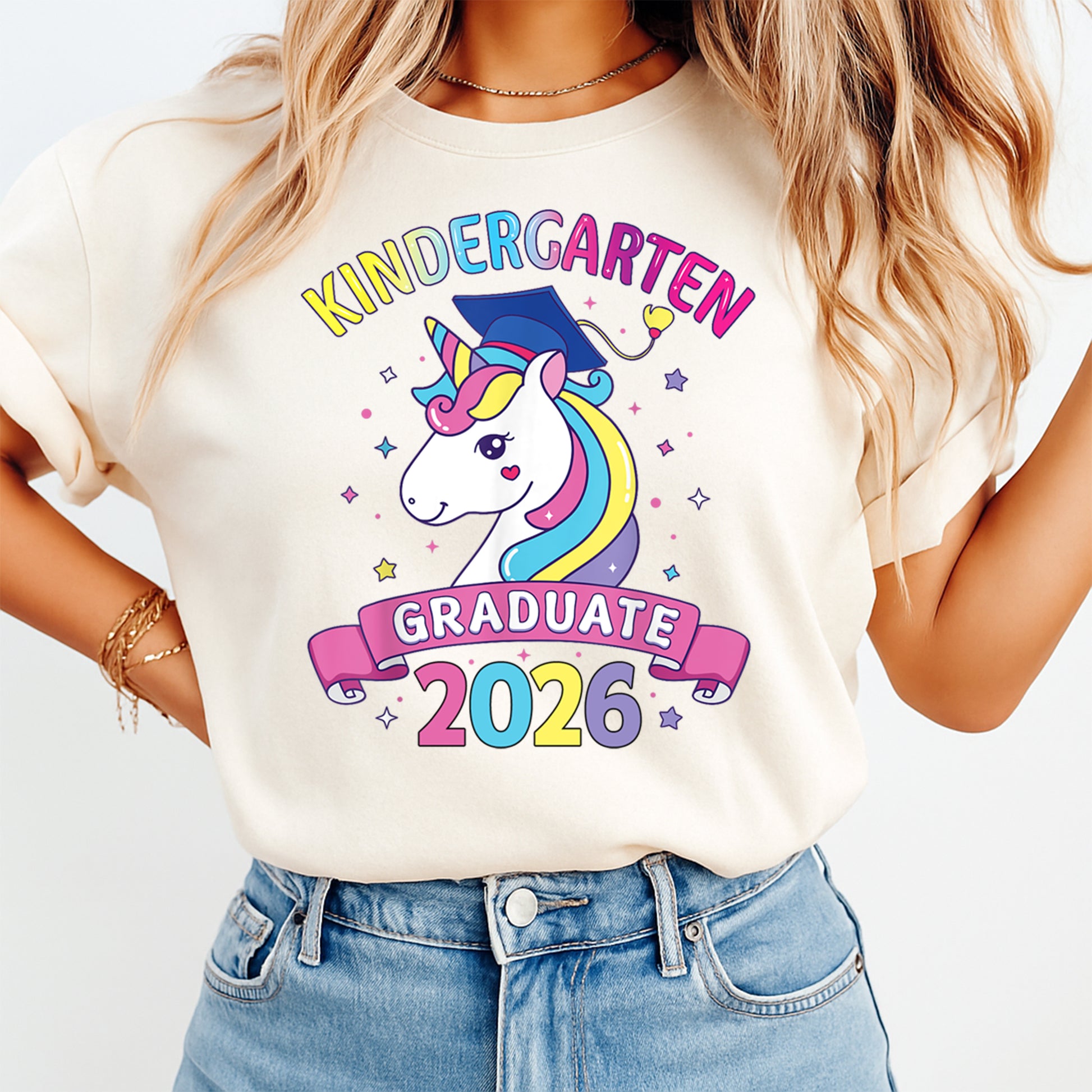 Cream shirt mockup featuring a Kindergarten Graduate 2026 ready to press dtf transfer with a pastel unicorn, graduation cap, stars, and pink banner.