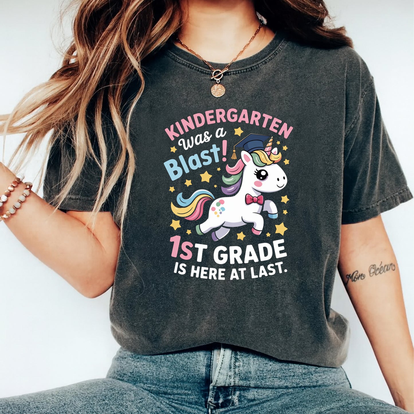 Black shirt mockup featuring a Kindergarten Was a Blast ready to press dtf transfer with unicorn, graduation cap, stars, and first grade text.