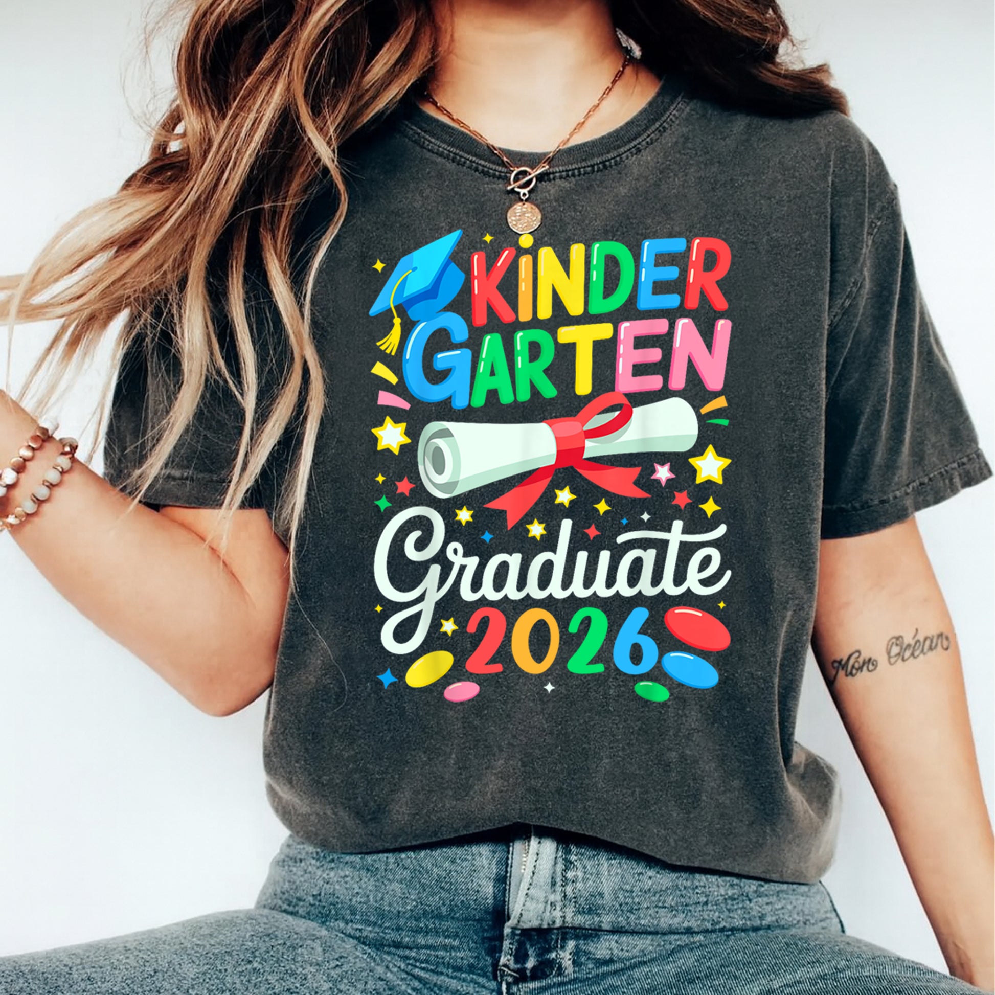 Black shirt mockup featuring a Kindergarten Graduate 2026 ready to press dtf transfer with colorful lettering, blue graduation cap, diploma, stars, and confetti.