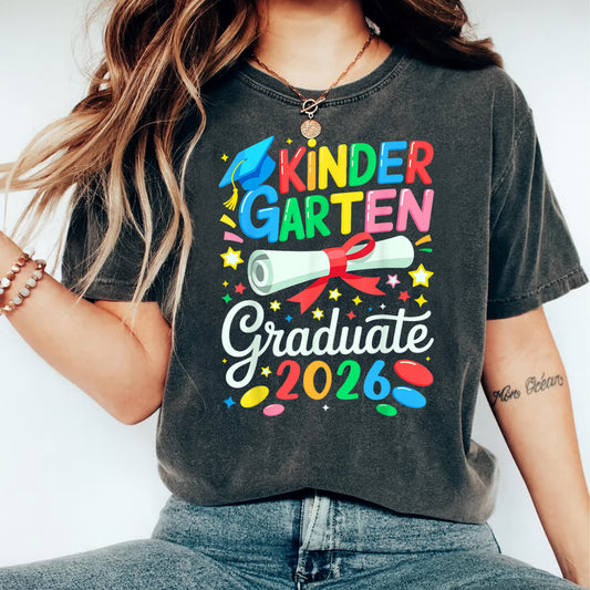 Black shirt mockup featuring a Kindergarten Graduate 2026 ready to press dtf transfer with colorful lettering, blue graduation cap, diploma, stars, and confetti.