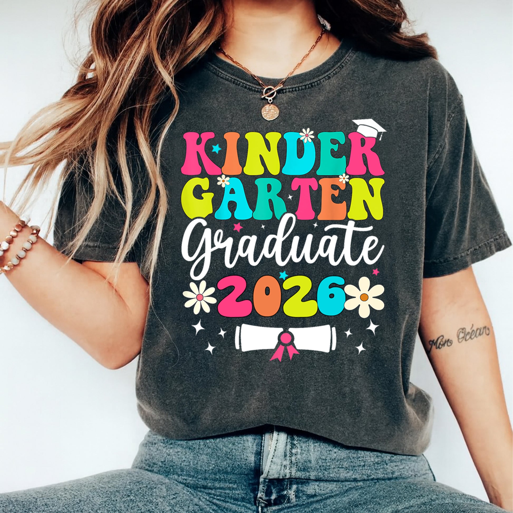 Black shirt mockup featuring a Kindergarten Graduate 2026 ready to press dtf transfer with colorful lettering, flowers, graduation cap, and diploma.