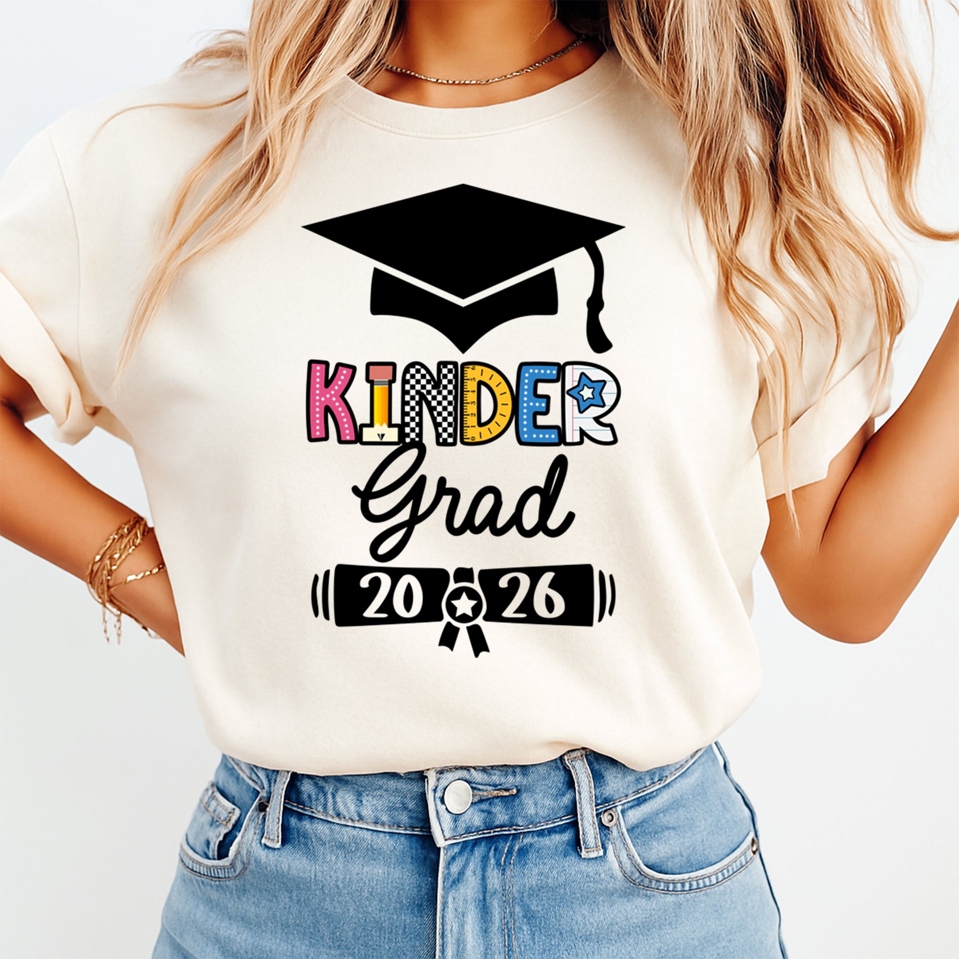 Cream shirt mockup featuring a Kinder Grad 2026 ready to press dtf transfer with graduation cap and colorful school lettering.